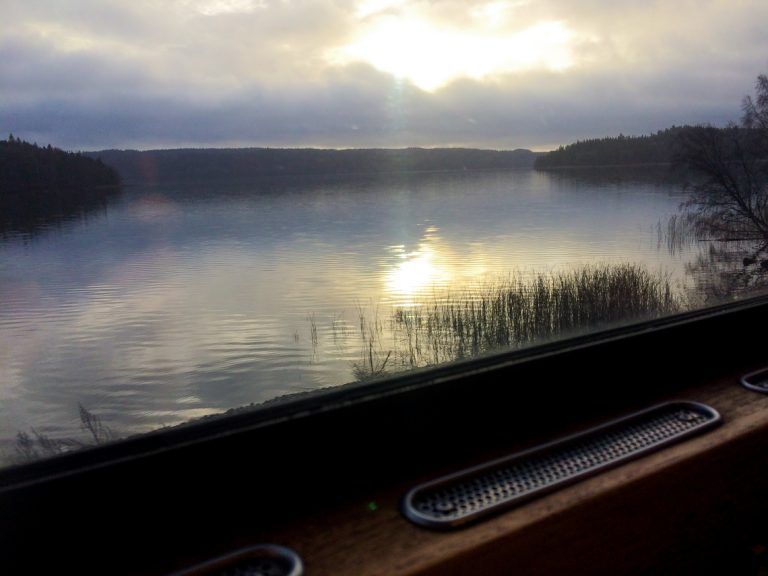 Utsikt fra et vindu i retrotoget til en speilblank svensk innsjø.