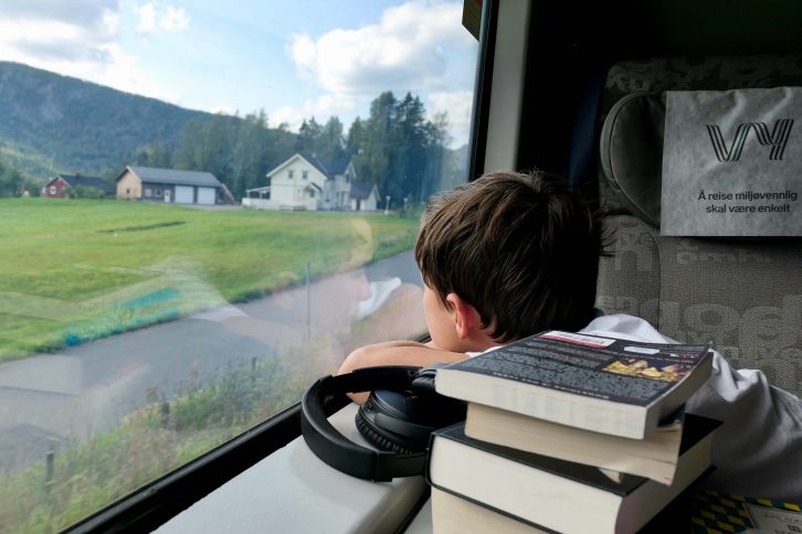 Ung passasjer på et fjerntog i Norge. Han har med seg bøker og podkaster, men ser likevel ut av vinduet.